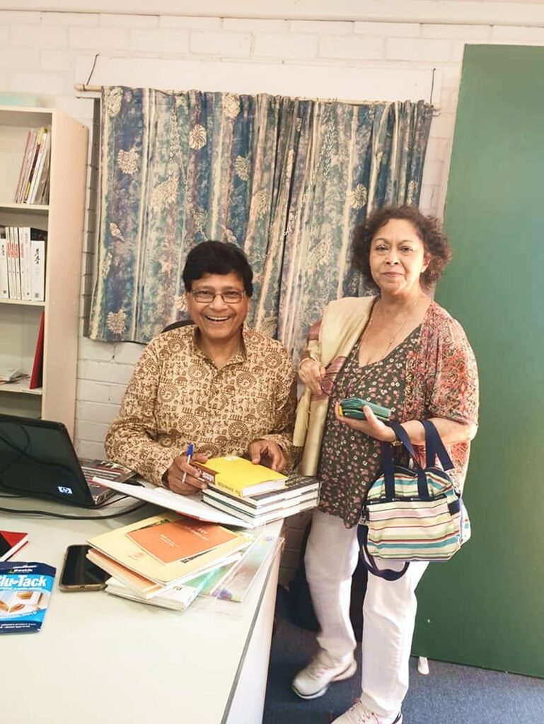Author signing books at an Anandodhara literary event, standing beside a guest