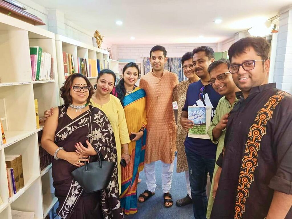 Anandodhara members gathered by a bookshelf holding a publication
