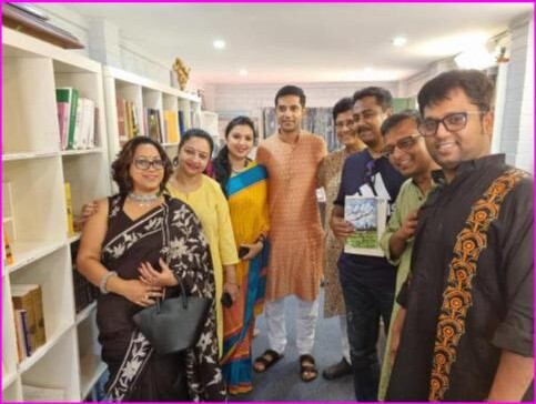 Anandodhara members gathered by a bookshelf holding a publication